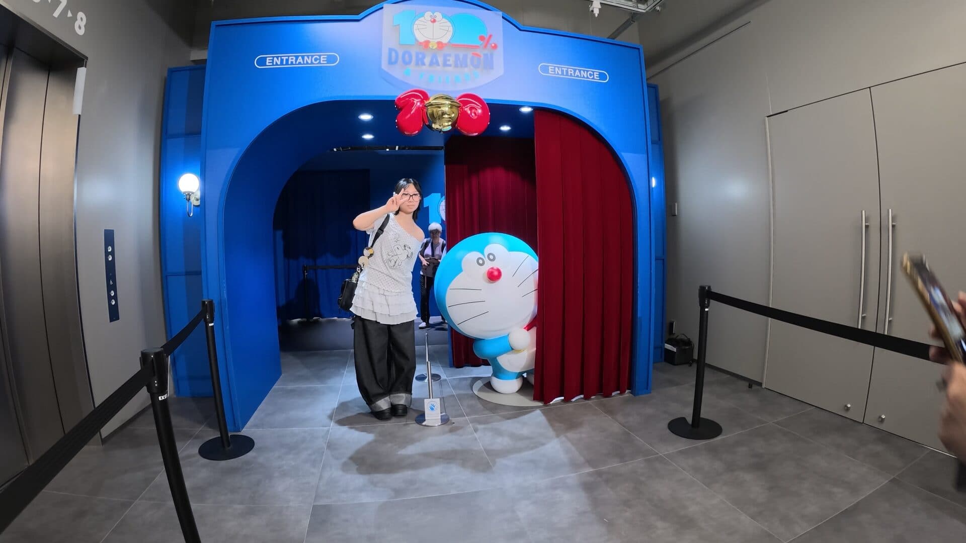 Blue ENTRANCE arch, red curtain, Doraemon peeking out, and gold bell balloons.