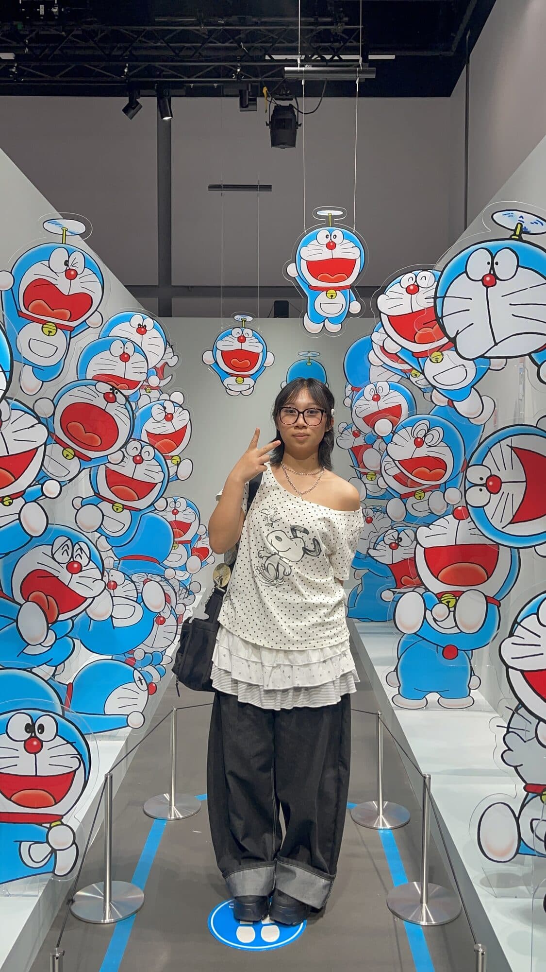 A woman in a polka-dot top among the hanging Doraemon faces.